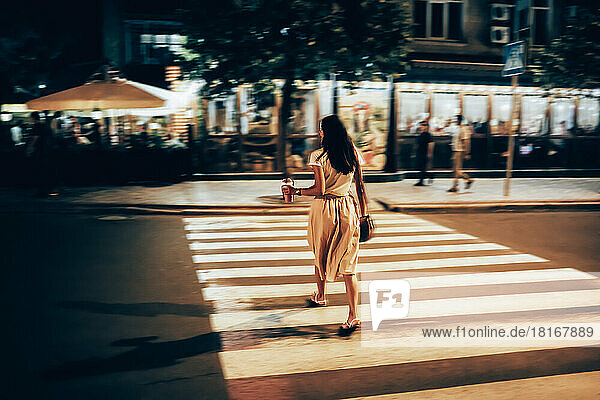 Woman with smoothie crossing street at night