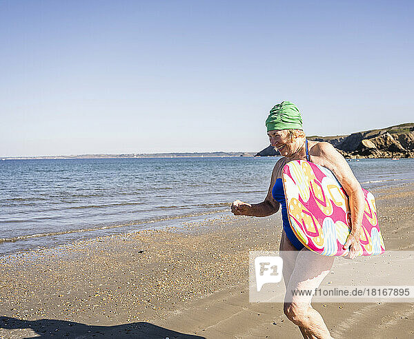 Ältere Frau mit Surfbrett  die Spaß am Strand hat