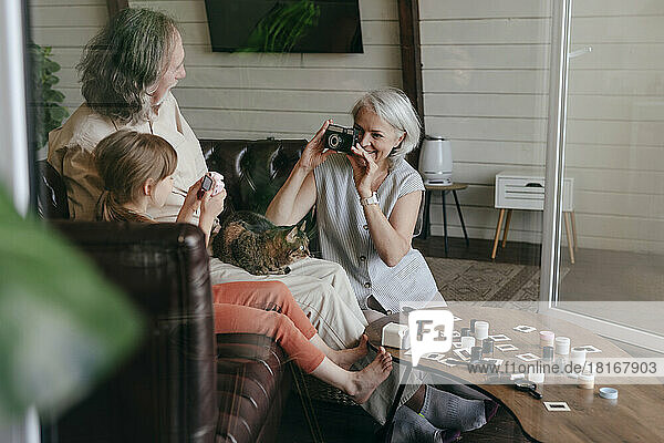 Woman taking photo of senior man and granddaughter on vintage film camera at home