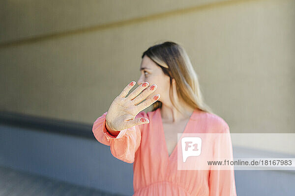 Woman gesturing stop sign with color on fingers in front of wall