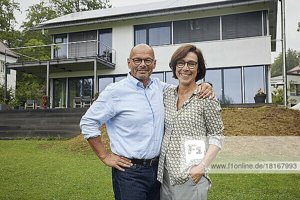Happy senior couple standing together in front of house