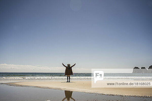 Woman standing with arms raised at shore on sunny day