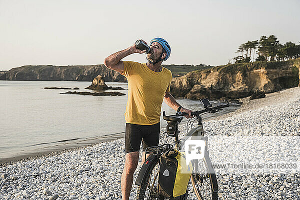 Mature man with bicycle drinking water at beach