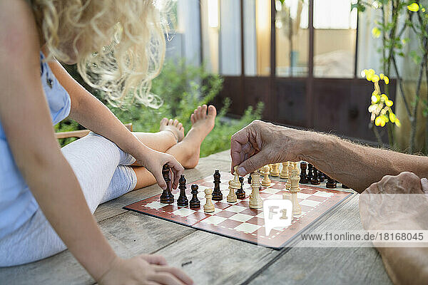 Die Hände des Großvaters spielen Schach mit der Enkelin auf dem Tisch
