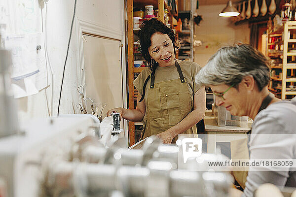 Smiling entrepreneur talking with colleague working at ceramics workshop