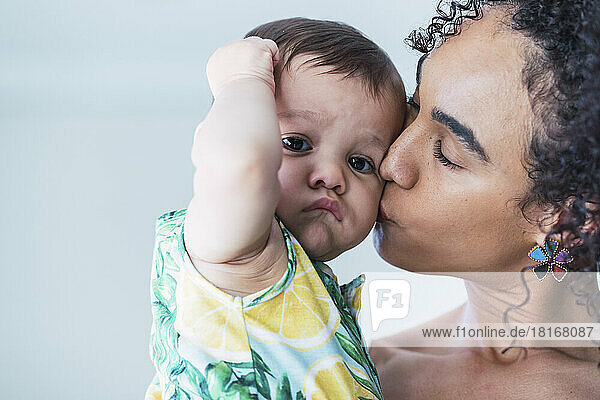 Mother kissing baby boy on cheek at home