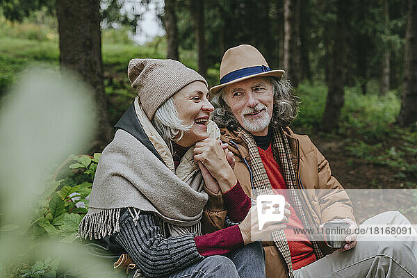 Smiling mature woman with senior man sitting in forest