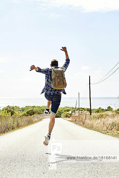 Backpacker with arms raised jumping on road