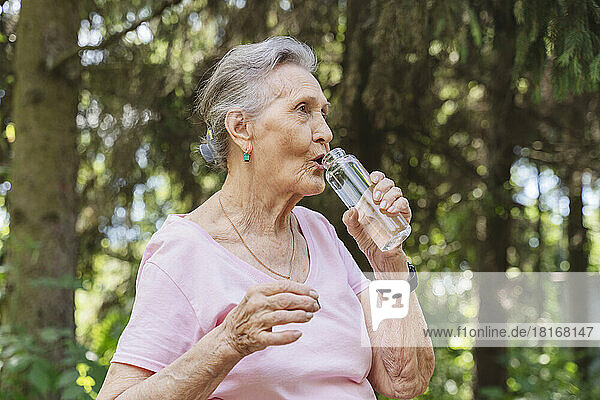 Senior woman drinking water through bottle at park