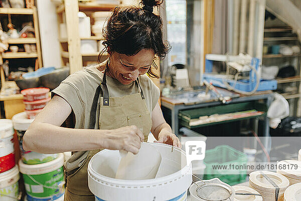Cheerful potter with bucket of clay working at ceramics workshop