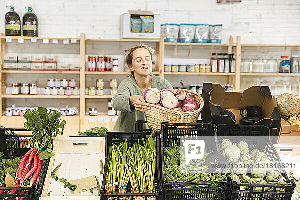 Woman holding basket of turnips in greengrocer shop