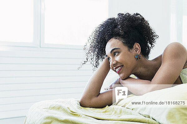 Thoughtful woman with curly hair lying on bed at home