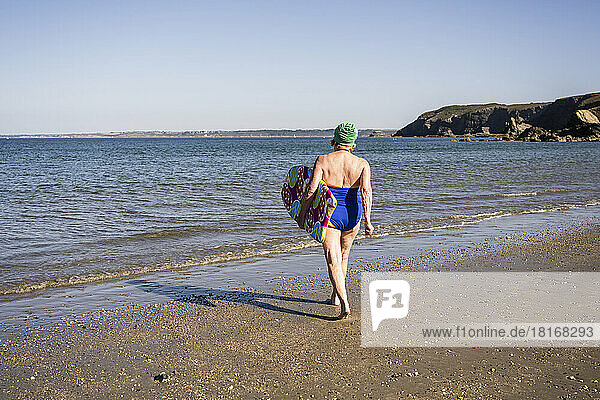 Woman with surfboard walking towards sea at beach
