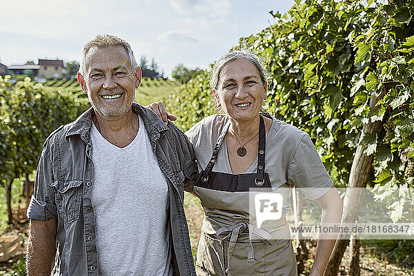 Happy mature farmers standing together at vineyard