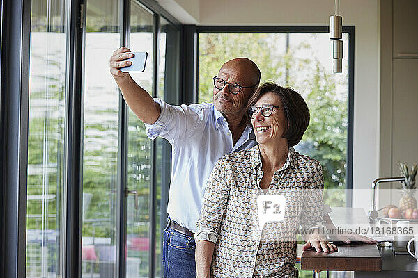 Happy senior woman with man taking selfie through smart phone at home
