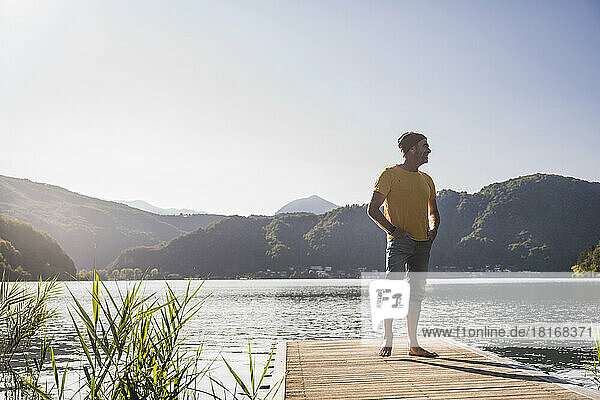 Smiling man with knit hat and hands in pockets on jetty over lake