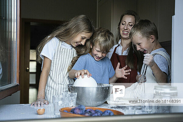 Glückliche Kinder  die zu Hause in der Küche von ihrer Mutter Teig zubereiten