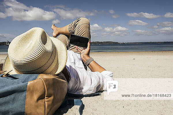 Mature woman using smart phone and relaxing at beach on sunny day