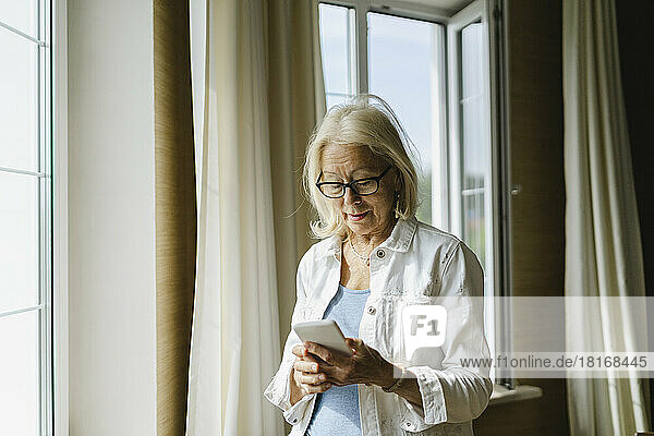 Woman with eyeglasses using mobile phone at home