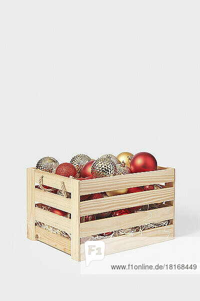 Wooden box full of colorful christmas baubles against white background