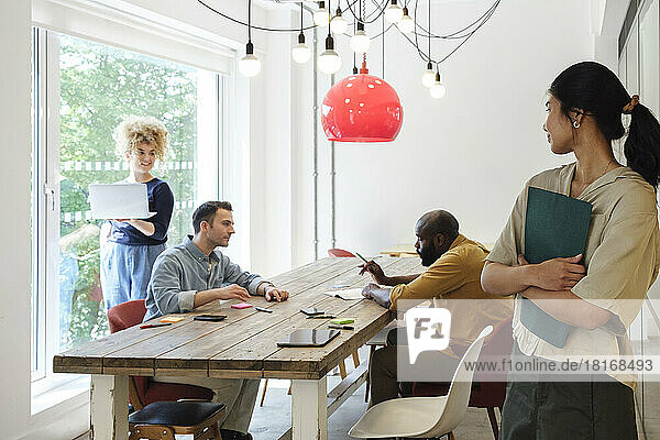 Young woman watching business people working together in modern coworking space