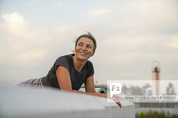 Smiling woman leaning on wall at sunset