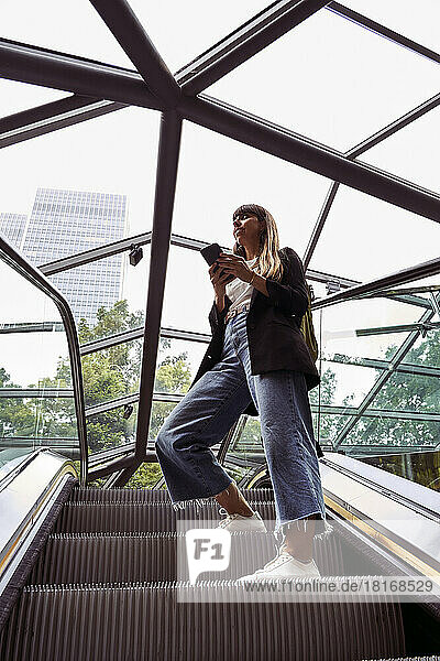 Frau mit Smartphone steht auf Rolltreppe
