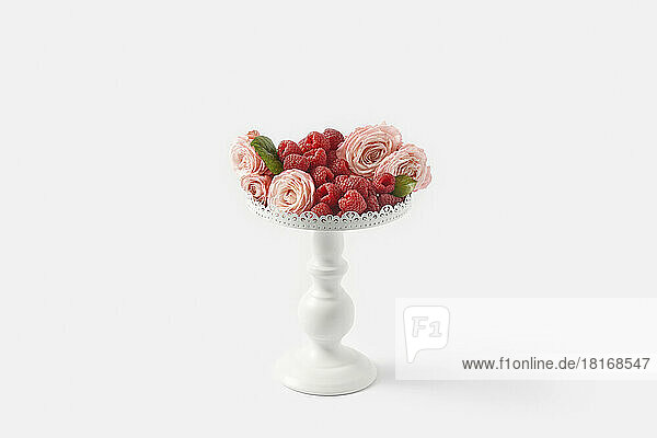 Raspberries with pink roses on pedestal cakestand against white background