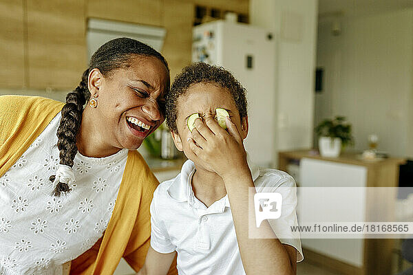 Glückliche Mutter umarmt ihren Sohn und bedeckt zu Hause die Augen mit Gurken