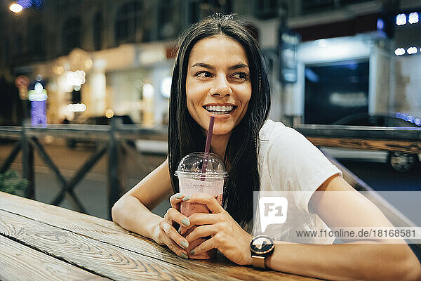 Happy beautiful woman with smoothie drink sitting at sidewalk cafe