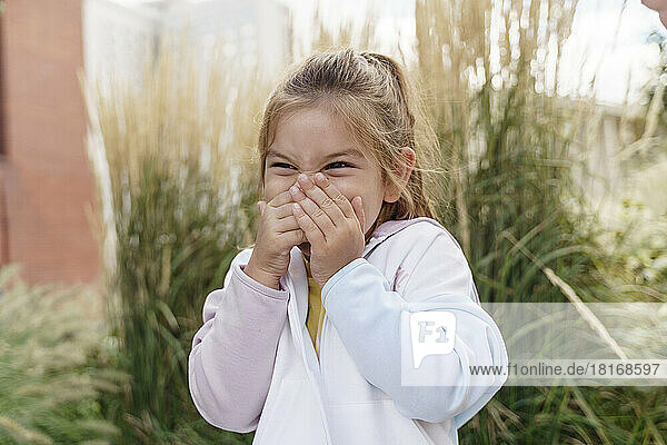 Happy girl covering mouth with hands in park