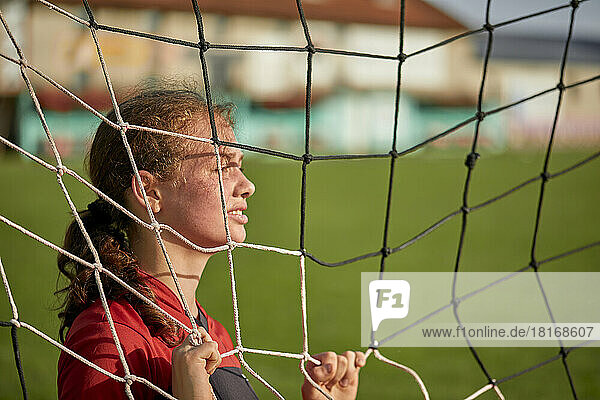Girl standing behind net on field on sunny day