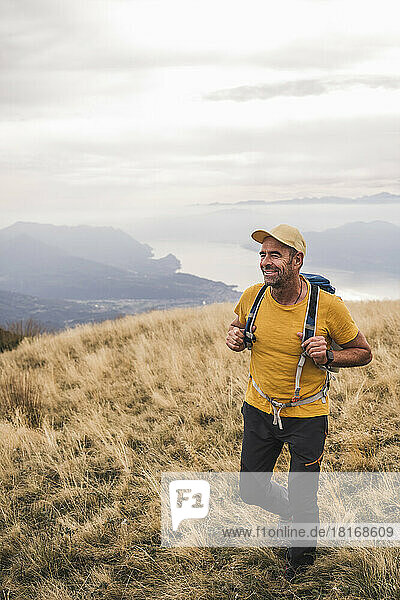 Lächelnder reifer Mann mit Mütze beim Wandern auf dem Berg