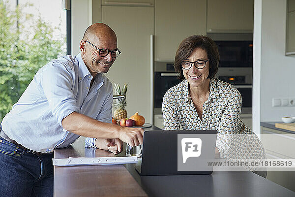 Happy man with woman using laptop on kitchen counter at home