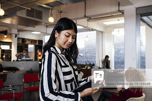 Young businesswoman standing in coworking office using digital tablet