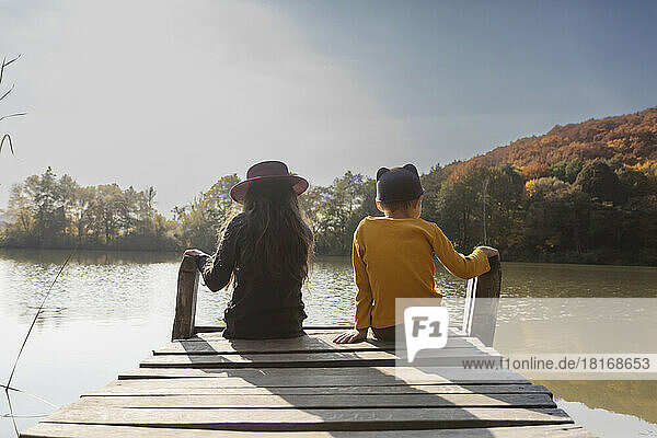 Boy and girl sitting on jetty at lake