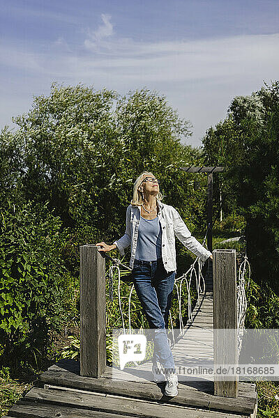 Senior woman enjoying sunlight standing on footbridge