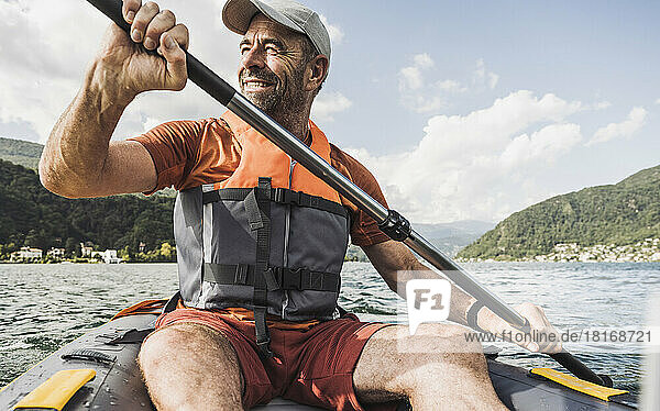 Lächelnder reifer Mann rudert an einem sonnigen Tag ein Kajakboot