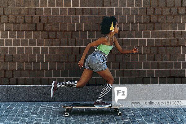 Woman longboard skating on footpath by wall
