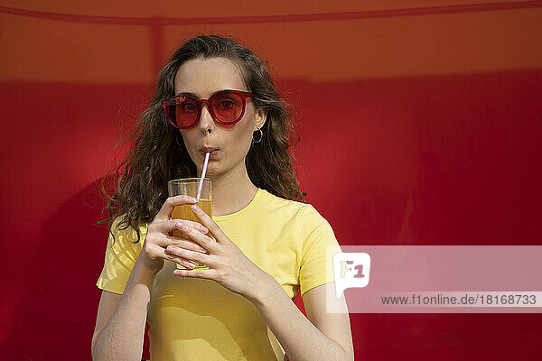 Woman drinking juice wearing sunglasses in front of red wall
