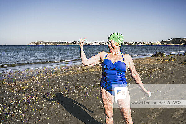 Frau zeigt Bizeps am Strand an einem sonnigen Tag