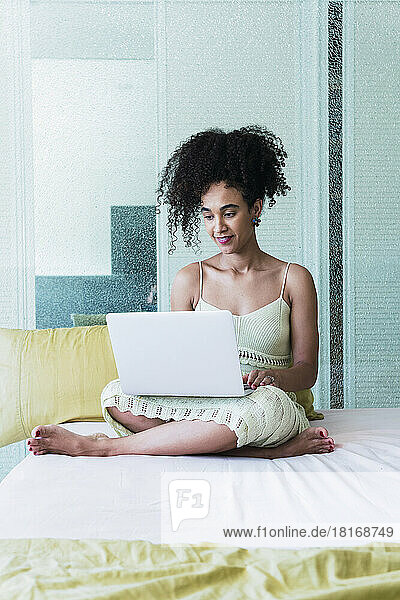 Curly-haired woman using laptop on bed at home