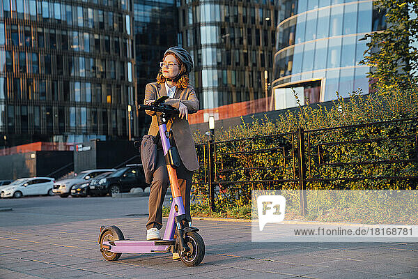 Thoughtful businesswoman with electric push scooter on street