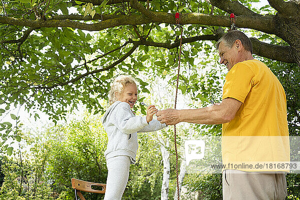 Grandfather and granddaughter making swing with rope in garden