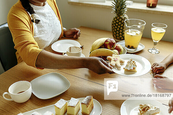Hand of woman holding plate of lemon meringue pie and gingerbread at dining table