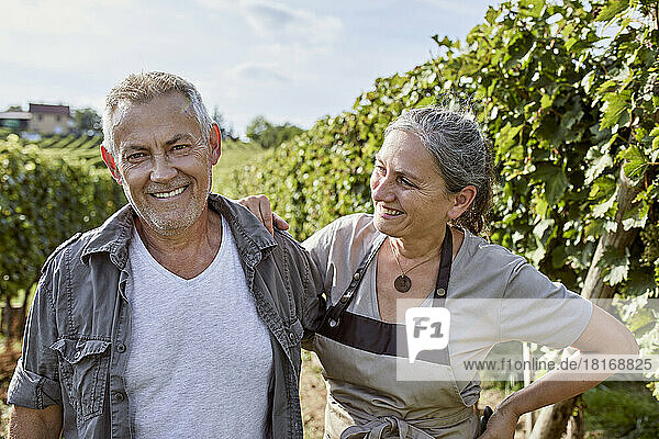 Happy farmer with hand on hip looking at man in vineyard
