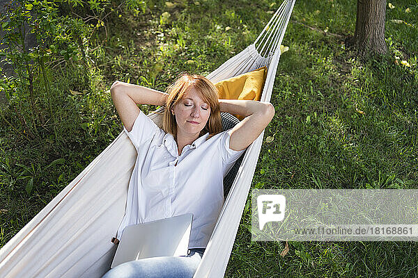 Freelancer lying with laptop in hammock at garden