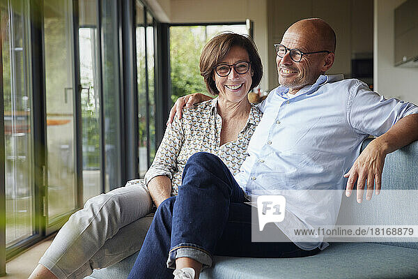 Fröhliches Seniorenpaar sitzt zu Hause gemeinsam auf dem Sofa