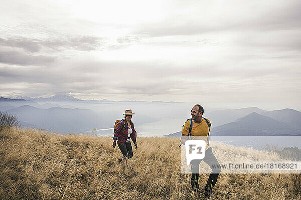 Happy mature couple hiking on mountain under cloudy sky