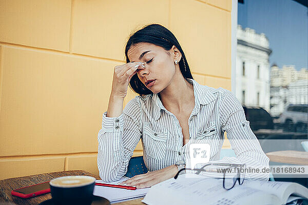 Stressed businesswoman with eyes closed sitting at table in sidewalk cafe